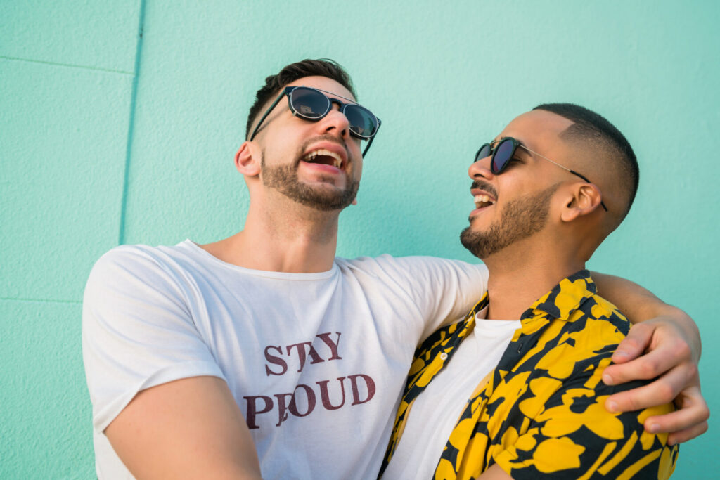 Twee mannen lachen samen en omhelzen elkaar, symbool voor verbinding, vreugde en jezelf kunnen zijn.